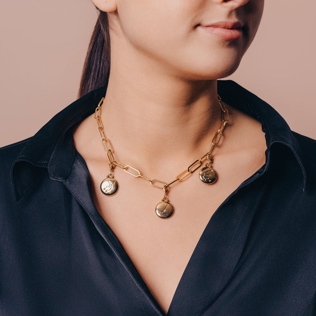 kvinnlig modell som bär på halsband med dubbelsidig guldpläterad berlock med stjärntecken.